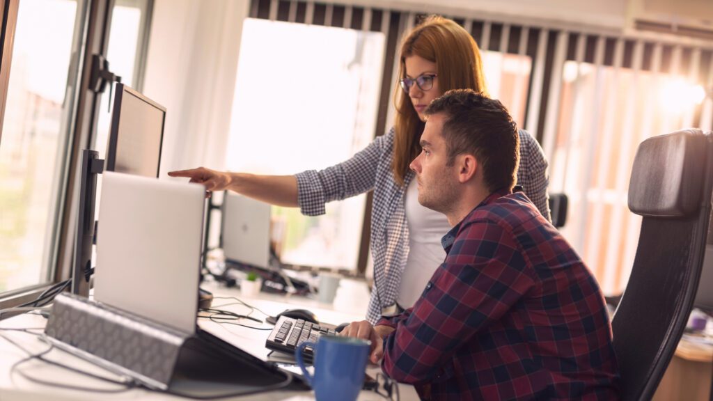 Dos profesionales colaborando en una oficina moderna, analizando información en una pantalla.